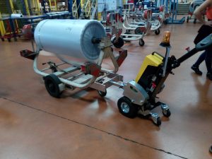 Electric pedestrian tow tug Alitrak AU LT300 moving a heavy wheeled trolley indoors.